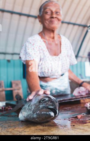 A woman smiles while selling a fresh fish at a market stall at the fish market in Negombo, Sri Lanka Stock Photo