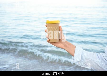 Woman holding paper coffee cup by the sea Stock Photo