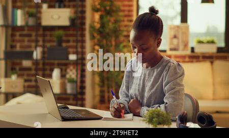 Freelancer taking notes about work, using notebook planner to help with remote job productivity at desk. African american woman writing down ideas as inspiration, home office. Stock Photo