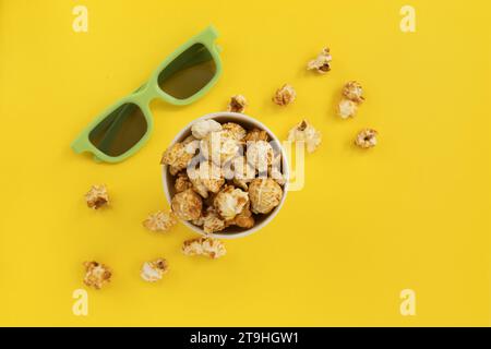 caramel popcorn in paper bucket and 3D glasses on yellow background, home cinema, top view Stock Photo