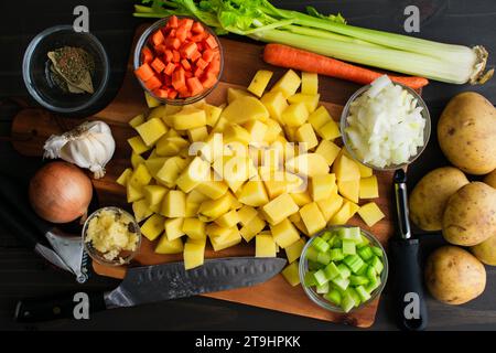 Chopped Yellow Potatoes Surrounded with Other Ingredients: Prepped potatoes, carrots, onions, celery, and garlic with kitchen utensils Stock Photo