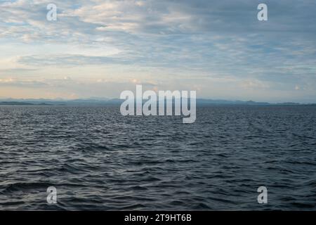 Coastline Seen From Afar with a Volcanic Mountain, Lush Vegetation Forest, Beach, and Houses with Small Waves on a Calm Ocean Stock Photo