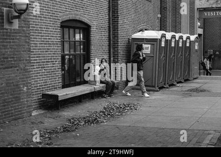 Salem, Massachusetts - A woman smiles with satisfaction alongside her package with an alien peeking out and her companion moving on from the row of po Stock Photo