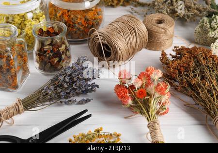 Different medicinal herbs, scissors and spools on white wooden table Stock Photo