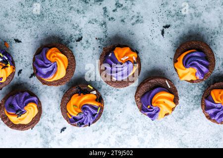 Brownie  chocolate cupcakes with ghost cream decor and sprinkles on a slate board on a gray background. Happy Halloween concept. American culture and Stock Photo