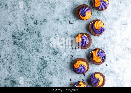 Brownie  chocolate cupcakes with ghost cream decor and sprinkles on a slate board on a gray background. Happy Halloween concept. American culture and Stock Photo
