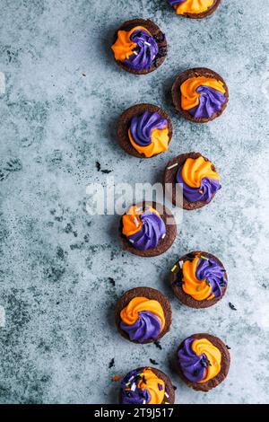 Brownie  chocolate cupcakes with ghost cream decor and sprinkles on a slate board on a gray background. Happy Halloween concept. American culture and Stock Photo