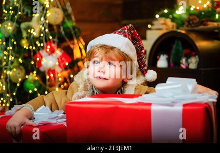Happy child holding a giant red gift box with both hands. Christmas kids. New year kids. Funny kid holding Christmas gift. Stock Photo