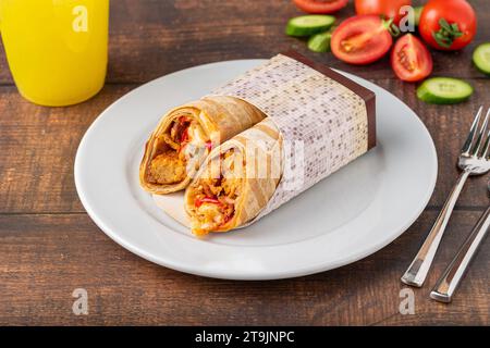 Chicken wrap with vegetables on a white porcelain plate on wooden table Stock Photo