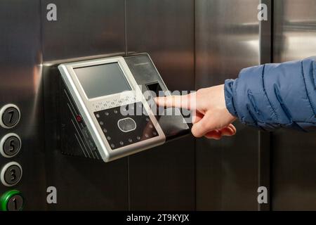 The man put his finger in the Fingerprint Access Control Terminal with face recognition function installed in the elevator of the business center, whi Stock Photo