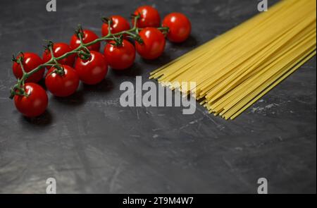 Cherry tomatoes branch and raw spaghetti - ingredients for making Italian pasta, on dark background, selective focus. Stock Photo