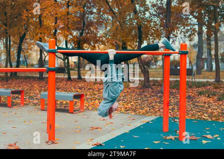 Young gymnast urban Caucasian woman at playground hanging upside down on bars and doing splits in park at autumn Stock Photo