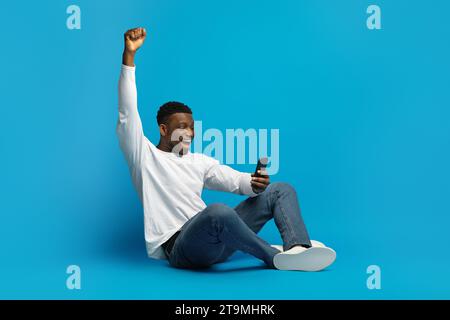 Excited Black Man Celebrating Win, Using Cellphone Stock Photo
