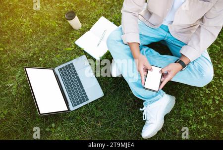 Asian man sitting on grass while using phone and laptop Stock Photo