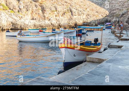 Blue Grotto, Malta - August 22, 2019: Coastal view with the Blue Grotto bay. Wooden boats are anchored at the pier on a sunny morning, people walk the Stock Photo