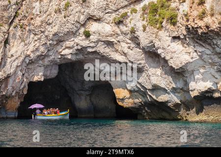 Blue Grotto, Malta - August 22, 2019: Coastal landscape with rocks and pleasure motor boat full of tourists sailing caves on a  sunny summer day Stock Photo