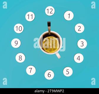 A mockup of a cup of tea and magnetic numbers in the shape of a round clock. Tea cup handle and spoon indicating five o'clock, on a simple light blue Stock Photo