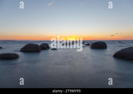 Sunset over the sea, orange strip of sunshine. Erratic boulders apperaring from the water. Stock Photo