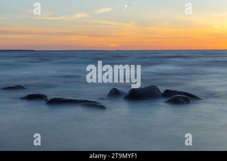 Sunset over the sea, orange strip of sunshine. Erratic boulders apperaring from the water. Stock Photo