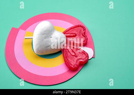 Two red heart-shaped lollipops on top of a rainbow with a pure white heart. Concept of pure love. Stock Photo