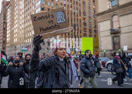 NEW YORK, NEW YORK - NOVEMBER 25: A pro-Palestine protester carries a sign that reads: 'Zionists vs. humanity' while marching to the American Museum of Natural History demanding a permanent ceasefire between Israel and Hamas during a protest dubbed the 'Anti-Colonial Tour' on November 25, 2023 in New York City. The Palestinian militant group Hamas launched a surprise attack on Israel from Gaza by land, sea, and air, last weekend, killing over 900 people and wounding more than 2000, recent agency reports said. Reports also said Israeli soldiers and civilians have been kidnapped by Hamas and tak Stock Photo