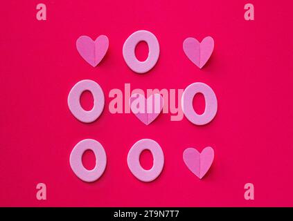 Tic tac toe made of hearts and zeros on pink background. Love always wins concept. Flat lay. Valentine's or love concept. Stock Photo