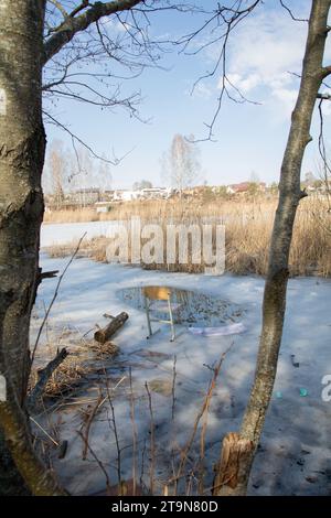 Photo on a lake covered with crusted ice is a chair and there is a hole in the ice for fishing, lake, day, atmosphere, active, relaxation, cold temper Stock Photo