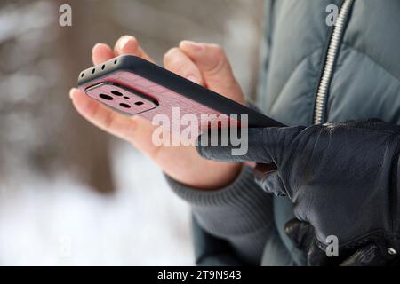 Female hands with smartphone close up on blurred background. Woman using mobile phone stands on a street in snow winter Stock Photo