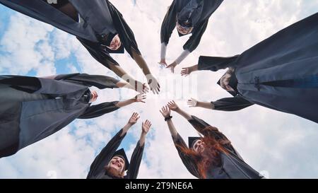 Team of college or university students celebrating graduation. Group of happy successful graduates in academic hats and robes standing in circle and Stock Photo