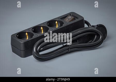 Electrical cord with three outlets and a power switch. Brand new black power cord with plugs, isolated on gray. Stock Photo