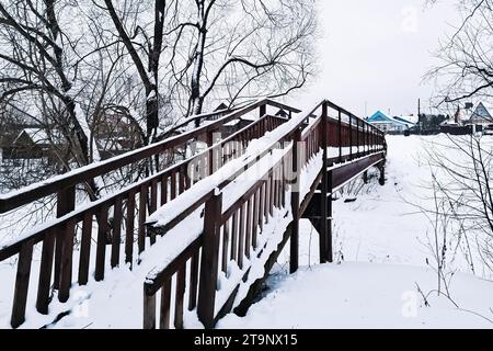Snow-covered wooden bridge in park on winter day. Footbridge covered with snow. Perspective Stock Photo