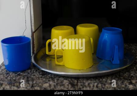 blue and yellow colored plastic cups on top of a metal tray. drinks and food. Stock Photo