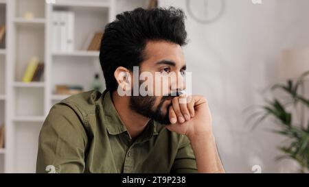Bored millennial generation man sitting on sofa, feeling lonely at home. Unhappy young male suffering from negative thoughts, having depressive mood Stock Photo