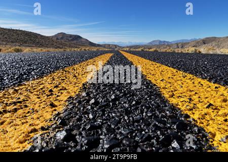 close up of a remote road and yellow lines leading off towards distant mountains Stock Photo