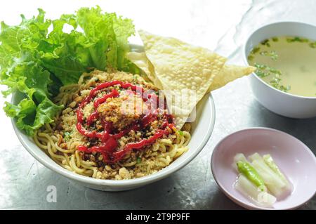 Mie ayam (noodles with chicken, meatballs, dumplings and vegetables) is a popular street food in Indonesia. Served in bowl on wooden table. Selected f Stock Photo