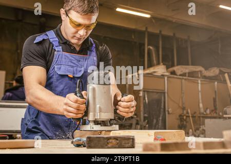 Male carpenter using electric sander to polish wooden plank in joinery workshop Stock Photo