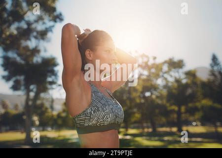 Close up shot of fitness model doing stretching workout at the park. Determined young woman wearing sports bar exercising on a sunny day. Stock Photo