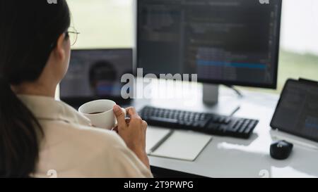 Developer programmer drinking coffee and checking code on monitor for programming to developing web. Stock Photo