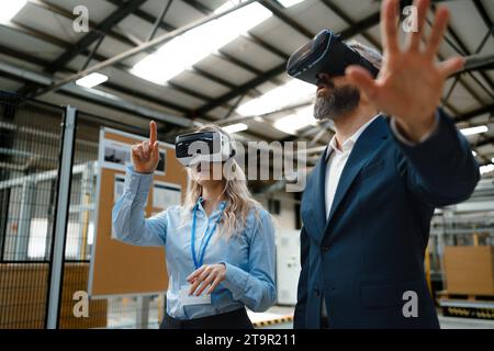 Engineers talking project using VR, in modern industrial factory. Virtual reality in manufacturing industry, Smart glasses guiding female and male Stock Photo