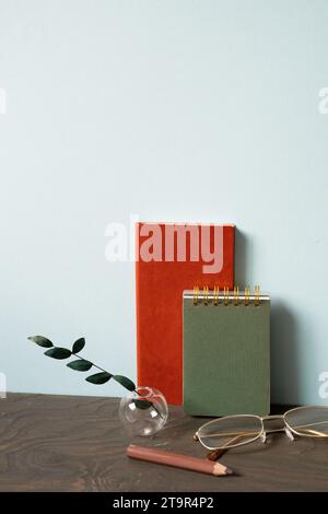 Office desk with diary note, eyeglasses, pencil, plant on wooden table. blue wall background Stock Photo