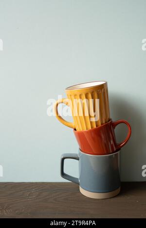 Stack of colorful ceramic mug cups on wooden table. blue wall background Stock Photo