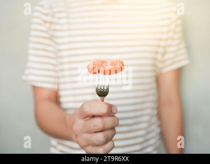 Front view of man in striped t shirt holding fork with carrot pieces on it in selective focus Stock Photo