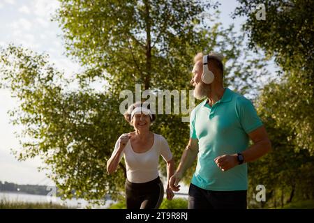 Lovely joyful retirees couple jogging outside in city park in morning Stock Photo