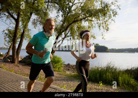 Happy elderly couple running on beach enjoying jogging workout in morning Stock Photo