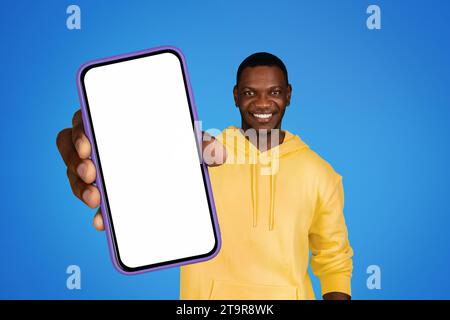 Smiling black man holds cellphone empty screen on blue background Stock Photo