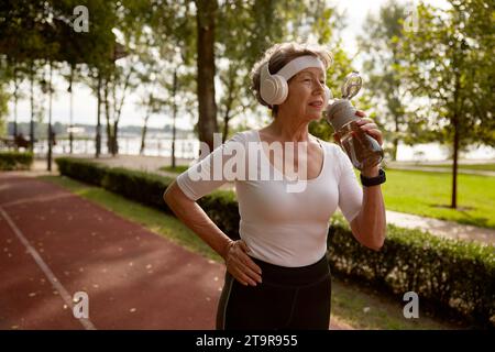Elderly woman drinking water taking short break during running exercise Stock Photo
