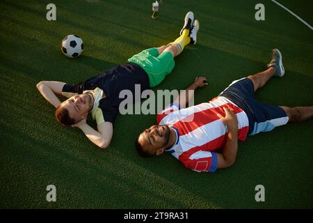 Smiling restful two football players lying on green field grass overhead view Stock Photo