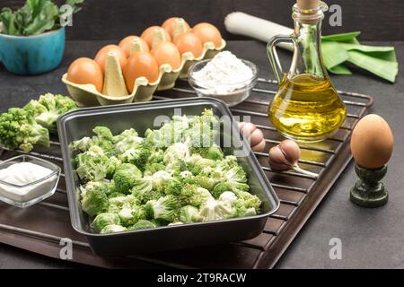 Mix broccoli and Brussels sprouts in food metal pallet. Eggs, garlic and onions, flour and butter in bottle on metal grill. Cooking casseroles. Black Stock Photo