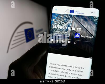 Person holding cellphone with webpage of EU financial institution European Investment Bank (EIB) with logo. Focus on center of phone display. Stock Photo