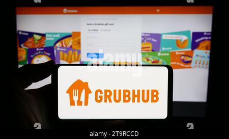 Person holding smartphone with logo of US food ordering and delivery company Grubhub Inc. in front of website. Focus on phone display. Stock Photo